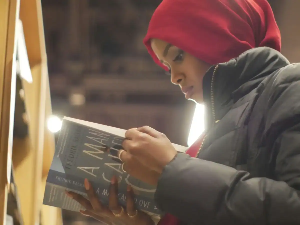 Focused young African woman in a red headscarf reading a book in a bookstore or library setting